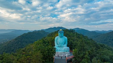 Bereketli ormanlarla çevrili, dingin bir Buda heykeli. Arka planda, sisli bir dağ manzarasının üzerine canlı renkler saçan çarpıcı bir gündoğumu. Gün doğumunda güzel gökyüzü. 