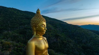 Gün batımının canlı renkleri sırasında yakalanan dingin bir vadiye bakan bir tepenin tepesindeki büyük altın Buda heykelinin hayranlık uyandırıcı görüntüsü. Lopburi Tayland 'daki en büyük altın Buda' nın hava manzarası.