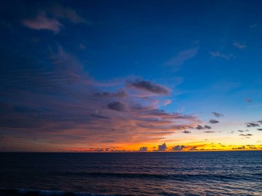 Canlı bir günbatımının büyüleyici bir görüntüsü. Gökyüzünde turuncu ve mor bir parıltı yayıyor. Hafif okyanus dalgaları kıyıya vuruyor.. 