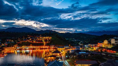 Baan Rak Thai Köyü, gün batımında Çin tarzı mimaride göl kenarındaki ev ve restoranların renkli ışıklarla yansıması.. 