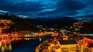 Baan Rak Thai Köyü, gün batımında Çin tarzı mimaride göl kenarındaki ev ve restoranların renkli ışıklarla yansıması.. 