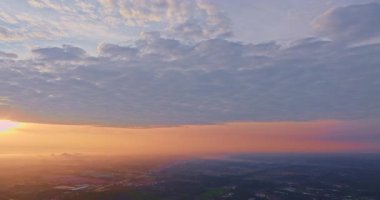 Sarı-turuncu gökyüzü bulutların ve sislerin arasında parlıyor.