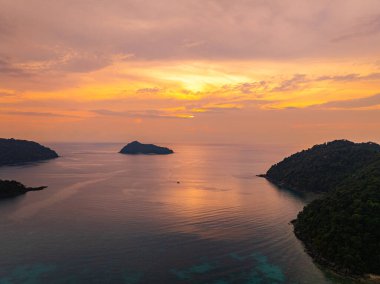 Gün batımında sakin okyanus sularıyla çevrili tropikal adaların nefes kesici bir görüntüsü. Gökyüzünün altın renkleri suyu yansıtıyor, sakin ve resimsi bir deniz manzarası yaratıyor. Surin Adası
