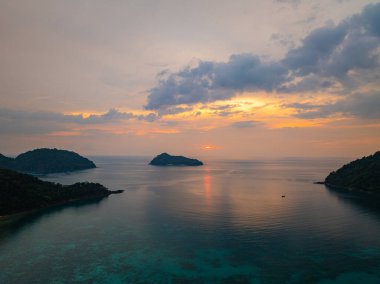 Güneşin Ao Mai Ngam, Surin Adaları 'ndan batışını gösteren hava manzarası. Batan güneşin yansıması. Bereketli yeşil tepeler ve demirlemiş yelkenlilerin silueti huzurlu ortamı geliştirirken.