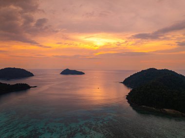 Surin Adaları 'ndaki Mai Ngam Plajı' ndaki tropikal bir sahil şeridinde gün batımının hava hiper yanılma görüntüsü. Gökyüzünün altın rengi suyu yansıtıyor, sakin ve resimsi bir deniz manzarası yaratıyor..