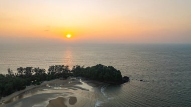 Gün batımında sakin okyanus sularına yansıyan altın rengi ile huzurlu bir sahil adasının çarpıcı hava manzarası. Ağaçların silueti ve kayalık oluşumlar huzur sahnesine derinlik katıyor..