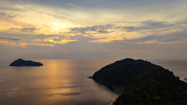Surin Adaları üzerinde çarpıcı bir günbatımının havadan görüntüsü. Sakin okyanus sularına yansıyan altın renklerle. Sahil şeridindeki mercan resifi derinlik katıyor. Şnorkel için cennet