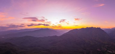 Sıcak turuncu, pembe ve mavi renkleri gökyüzünde pürüzsüz bir şekilde harmanlanmış, katmanlanmış dağ siluetlerinin üzerinde renkli bir günbatımının nefes kesici bir görüntüsü..
