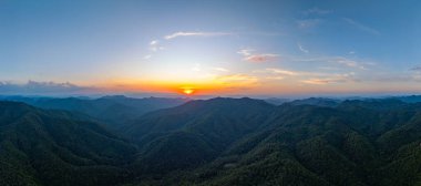 Güneşin doğuşunda bulutları mavi gökyüzüne doğru aydınlatan parlak turuncu ve pembe renkler ile çarpıcı bir dağ manzarası. Sis tabakası vadiye yerleşmiş, manzaraya rüya gibi bir manzara katmış..
