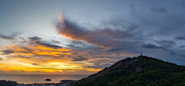 Phuket, Tayland 'daki Andaman Denizi' ne bakan ikonik Büyük Buda heykelinin canlı bir günbatımında çekilmiş nefes kesici bir görüntüsü. Altın gökyüzü suyu yansıtır. Güzel güneş