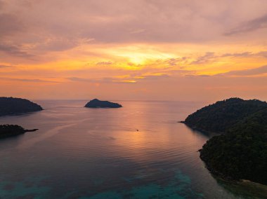 Gün batımında sakin okyanus sularıyla çevrili tropikal adaların nefes kesici bir görüntüsü. Gökyüzünün altın renkleri suyu yansıtıyor, sakin ve resimsi bir deniz manzarası yaratıyor. Surin Adası