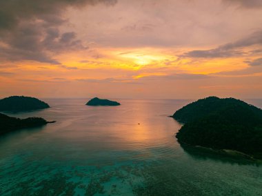 Surin Adaları 'ndaki Mai Ngam Plajı' ndaki tropikal bir sahil şeridinde gün batımının hava hiper yanılma görüntüsü. Gökyüzünün altın rengi suyu yansıtıyor, sakin ve resimsi bir deniz manzarası yaratıyor..