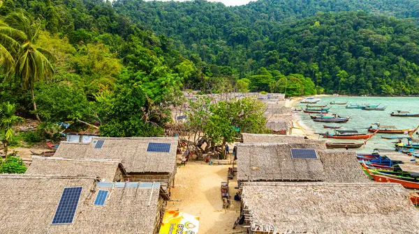 Phang Nga, Tayland-Mart, 20.2025: Yeşillik yeşil ormanlarla çevrili kıyı şeridi boyunca sıralanmış küçük kulübeleriyle tropikal bir sahil Morgan köyünün çarpıcı hava manzarası. Balıkçı tekneleri demirli.