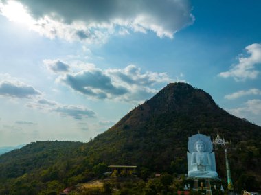 Görkemli bir Buda heykeli yemyeşil tepeler ve doğal ışık arasında meditasyon yapıyor. Bu huzurlu yer, kutsal mimarinin ve doğal güzelliğin uyumunu sergiliyor. dağ arkaplanı