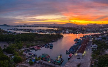 Phuket 'teki balıkçı limanında sersemletici gün batımını gösteren hava manzarası. Yumuşak mor renkten ateşli turuncu renklere dönüşen canlı gökyüzü, sakin ve pitoresk bir atmosfer yaratır..  