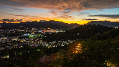 Gün batımında yemyeşil dağların arasında yuva yapmış, tepenin yamacına tünemiş bir kule ve sıcak, sakin bir turuncu gökyüzü manzarası..