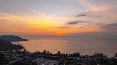 Phuket, Tayland 'daki Kata Sahili' nin gün batımında çekilen nefes kesici hava görüntüsü. Görüntü kıyı şeridini, küçük adaları, yemyeşil tepeleri ve parlak bir gökyüzünün altındaki canlı şehri gösteriyor.
