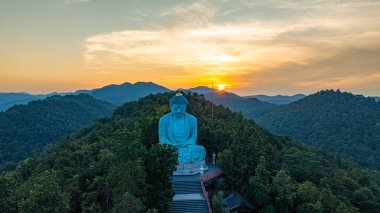 Bereketli ormanlarla çevrili, dingin bir Buda heykeli. Arka planda, sisli bir dağ manzarasının üzerine canlı renkler saçan çarpıcı bir gündoğumu. Gün doğumunda güzel gökyüzü. 