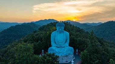 Bereketli ormanlarla çevrili, dingin bir Buda heykeli. Arka planda, sisli bir dağ manzarasının üzerine canlı renkler saçan çarpıcı bir gündoğumu. Gün doğumunda güzel gökyüzü. 