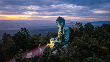 Bereketli ormanlarla çevrili, dingin bir Buda heykeli. Arka planda, sisli bir dağ manzarasının üzerine canlı renkler saçan çarpıcı bir gündoğumu. Gün doğumunda güzel gökyüzü. 