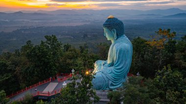 Bereketli ormanlarla çevrili, dingin bir Buda heykeli. Arka planda, sisli bir dağ manzarasının üzerine canlı renkler saçan çarpıcı bir gündoğumu. Gün doğumunda güzel gökyüzü. 