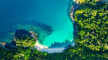 Berrak turkuaz suları, yemyeşil bitki örtüsü ve kayalık uçurumlarla çevrili tenha bir Özgürlük plajının nefes kesici hava manzarası. El değmemiş beyaz kum ve canlı okyanus renkleri