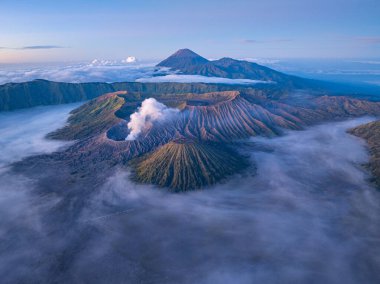 Bromo Dağı 'nın hava manzarası. Etrafı sis ve dramatik manzaralarla çevrili. Endonezya 'da aktif bir volkan yumuşak sabah ışığı engebeli araziyi ve yükselen volkanik dumanı aydınlatıyor.