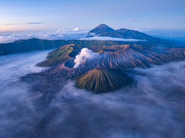 Bromo Dağı 'nın nefes kesici hava manzarası Endonezya' da aktif bir volkan, sis ve dramatik manzaralarla çevrili. Yumuşak sabah ışığı engebeli araziyi ve yükselen volkanik alanı vurguluyor. 