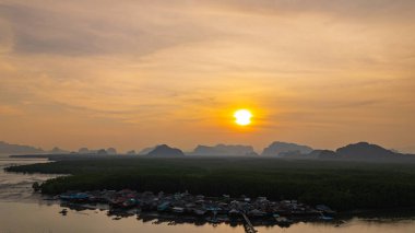 Bereketli mangrovlarla çevrili yüzen bir köyün nefes kesici hava manzarası. Güneş uzak kireçtaşı dağlarının ardında batıyor. Altın ışık sakin suları yansıtır. Bangpat Adası