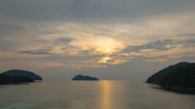 Surin Adaları üzerinde çarpıcı bir günbatımının havadan görüntüsü. Sakin okyanus sularına yansıyan altın renklerle. Sahil şeridindeki mercan resifi derinlik katıyor. Şnorkel için cennet