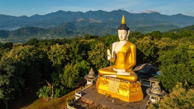 Etrafı yemyeşil ağaçlarla çevrili altın bir Buda heykelinin havadan görünüşü çarpıcı bir zemin ve berrak mavi bir gökyüzü üzerine kurulmuş. Ruhun ve doğanın ahengi. Fang kaplıcası.