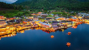 Baan Rak Tayland Köyü, gün batımında Çin tarzı mimaride göl kenarındaki ev ve restoranların renkli ışıklarla yansıması. Mae Hong Son 'da popüler bir turizm merkezi.