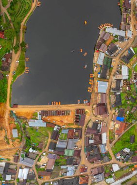 Göl kenarındaki bir köyün havadan görünüşü, kırsal mimari, yemyeşil ve sakin sulara dağılmış teknelerin karışımı sergileniyor. Doğal güzellik ve insan yerleşiminin ahenkli bir karışımı.