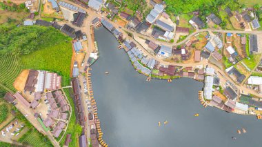 Göl kenarındaki bir köyün havadan görünüşü, kırsal mimari, yemyeşil ve sakin sulara dağılmış teknelerin karışımı sergileniyor. Doğal güzellik ve insan yerleşiminin ahenkli bir karışımı.
