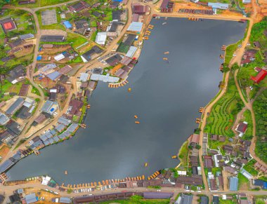 Göl kenarındaki bir köyün havadan görünüşü, kırsal mimari, yemyeşil ve sakin sulara dağılmış teknelerin karışımı sergileniyor. Doğal güzellik ve insan yerleşiminin ahenkli bir karışımı.