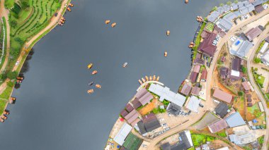 Göl kenarındaki bir köyün havadan görünüşü, kırsal mimari, yemyeşil ve sakin sulara dağılmış teknelerin karışımı sergileniyor. Doğal güzellik ve insan yerleşiminin ahenkli bir karışımı.