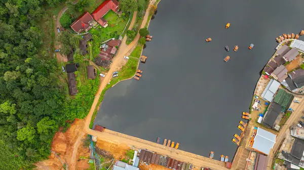 Göl kenarındaki bir köyün havadan görünüşü, kırsal mimari, yemyeşil ve sakin sulara dağılmış teknelerin karışımı sergileniyor. Doğal güzellik ve insan yerleşiminin ahenkli bir karışımı.