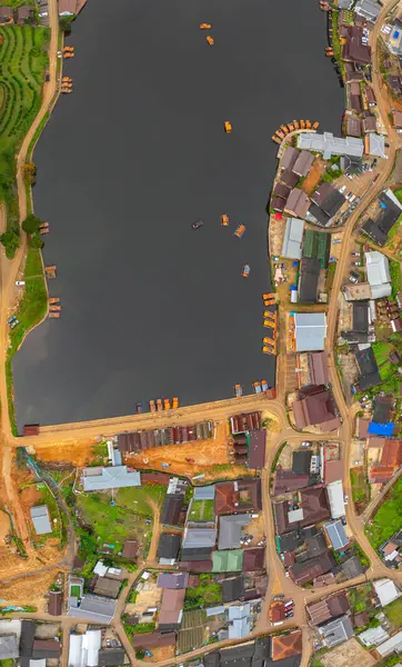 Göl kenarındaki bir köyün havadan görünüşü, kırsal mimari, yemyeşil ve sakin sulara dağılmış teknelerin karışımı sergileniyor. Doğal güzellik ve insan yerleşiminin ahenkli bir karışımı.