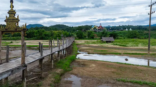 Tepe kabilesinin köyündeki muhteşem güzelliğin havadan görünüşü. Pilav tarlalarından geçen köprü ruhban sınıfıyla cemaati birbirine bağlayan Mae Hong Son 'un en uzun ve en güzel bambu köprülerinden biridir.