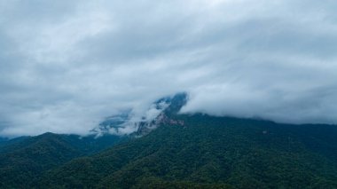 Yoğun bulutlarla kaplanmış gür, gür bir dağ zirvesinin dramatik manzarası, bulutlu bir gökyüzü altında doğanın saf güzelliğini ve gizemini yakalıyor..
