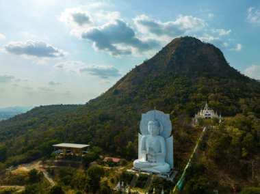 Görkemli bir Buda heykeli yemyeşil tepeler ve doğal ışık arasında meditasyon yapıyor. Bu huzurlu yer, kutsal mimarinin ve doğal güzelliğin uyumunu sergiliyor. dağ arkaplanı