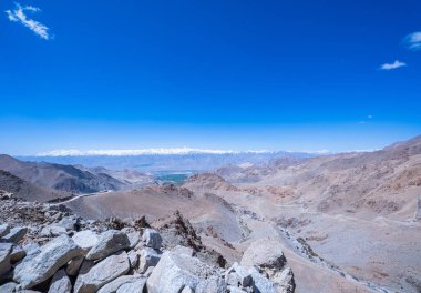 Karla kaplı tepeler ve derin mavi gökyüzü. Himalayalar üzerinde beyaz bulutlar süzülür. Kar ve kayalık yamaçlar arasındaki zıtlık dramatik dokuları vurgular. Dağların güzel doğası 