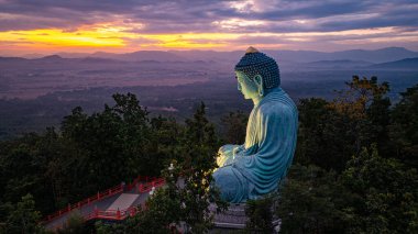Bereketli ormanlarla çevrili, dingin bir Buda heykeli. Arka planda, sisli bir dağ manzarasının üzerine canlı renkler saçan çarpıcı bir gündoğumu. Gün doğumunda güzel gökyüzü. 