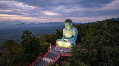 Bereketli ormanlarla çevrili, dingin bir Buda heykeli. Arka planda, sisli bir dağ manzarasının üzerine canlı renkler saçan çarpıcı bir gündoğumu. Gün doğumunda güzel gökyüzü. 