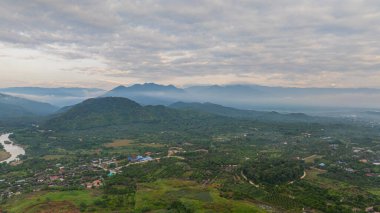 Şafak vakti geniş bir kırsal alanda akan dolambaçlı bir nehrin çarpıcı hava manzarası. Yumuşak sabah ışığı ve sisli atmosfer dağınık köylerle sakin ve resim gibi bir manzara yaratır.