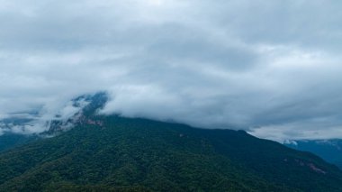 Yoğun bulutlarla kaplanmış gür, gür bir dağ zirvesinin dramatik manzarası, bulutlu bir gökyüzü altında doğanın saf güzelliğini ve gizemini yakalıyor..