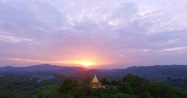 Güneşin batışında yemyeşil tepelerin arasında altın bir pagoda manzarası sersemletici.