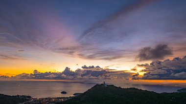 Nefes kesen bir gün batımının hava hiper yanılma görüntüsü sahneyi çevreleyen yemyeşil tepelerle dolu kıyı kasabasının üzerinde turuncu ve mavi renkli gökyüzünü resmediyor. Okyanusun üzerinde dramatik gün batımı bulutu