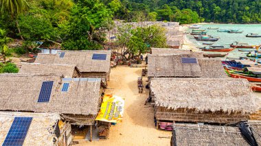 Phang Nga, Tayland-Mart, 20.2025: Yeşillik yeşil ormanlarla çevrili kıyı şeridi boyunca sıralanmış küçük kulübeleriyle tropikal bir sahil Morgan köyünün çarpıcı hava manzarası. Balıkçı tekneleri demirli.