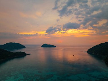Gün batımında sakin okyanus sularıyla çevrili tropikal adaların nefes kesici bir görüntüsü. Gökyüzünün altın renkleri suyu yansıtıyor, sakin ve resimsi bir deniz manzarası yaratıyor. Surin Adası